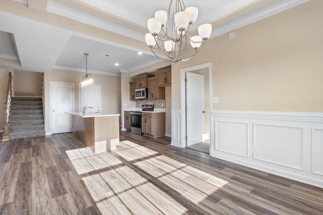 kitchen with dark wood-type flooring, stainless steel appliances, crown molding, an island with sink, and pendant lighting