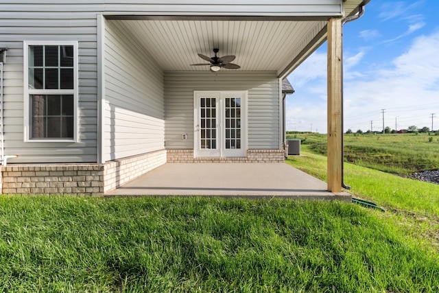 view of exterior entry with central AC unit, ceiling fan, a patio area, and a yard