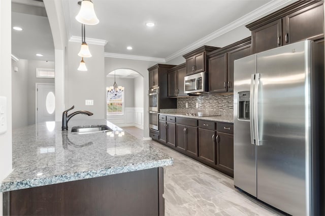 kitchen with sink, hanging light fixtures, appliances with stainless steel finishes, light stone counters, and dark brown cabinetry