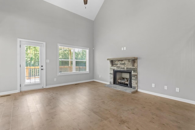 unfurnished living room with a stone fireplace, ceiling fan, high vaulted ceiling, and light hardwood / wood-style floors