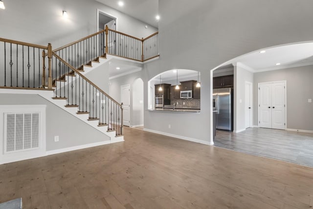 unfurnished living room with sink, wood-type flooring, crown molding, and a towering ceiling