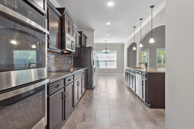 kitchen featuring backsplash, hanging light fixtures, appliances with stainless steel finishes, dark brown cabinets, and light stone counters