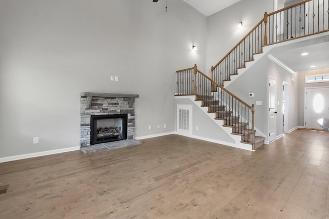 unfurnished living room featuring hardwood / wood-style floors, ceiling fan, a stone fireplace, and a towering ceiling