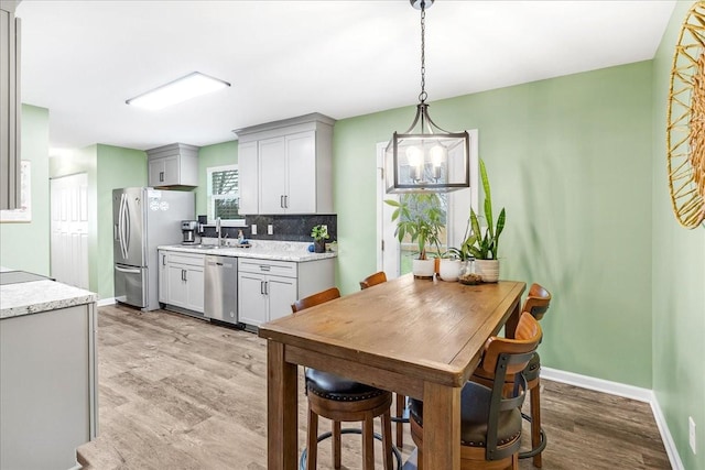 kitchen with tasteful backsplash, gray cabinetry, stainless steel appliances, light hardwood / wood-style floors, and hanging light fixtures