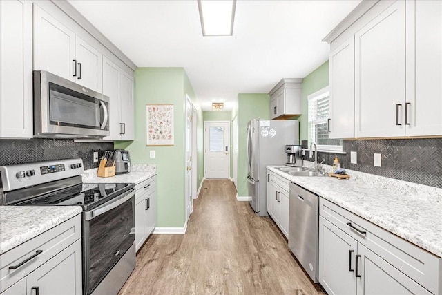 kitchen with appliances with stainless steel finishes, backsplash, sink, light hardwood / wood-style flooring, and white cabinets