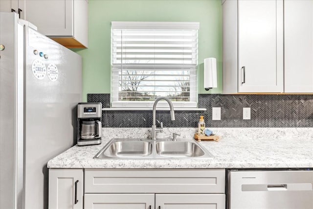 kitchen with decorative backsplash, stainless steel dishwasher, sink, white cabinetry, and fridge