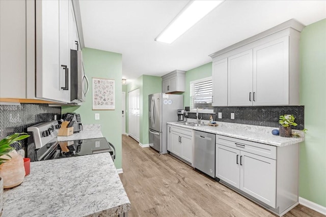 kitchen featuring light stone countertops, appliances with stainless steel finishes, light hardwood / wood-style floors, and sink