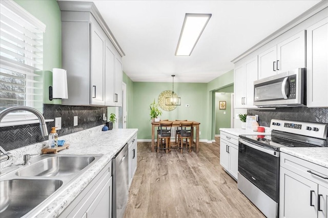 kitchen with sink, stainless steel appliances, light hardwood / wood-style flooring, pendant lighting, and white cabinets