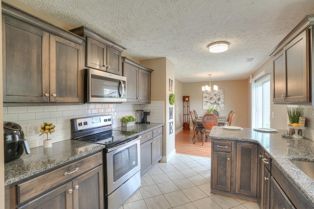 kitchen with appliances with stainless steel finishes, tasteful backsplash, light tile patterned floors, and dark stone counters