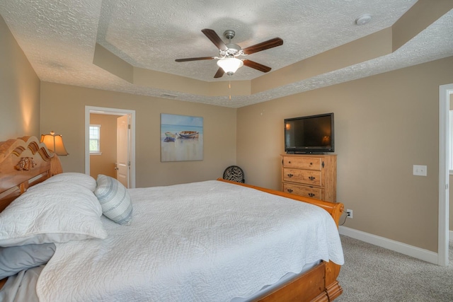 bedroom with carpet flooring, ensuite bath, a textured ceiling, a raised ceiling, and ceiling fan