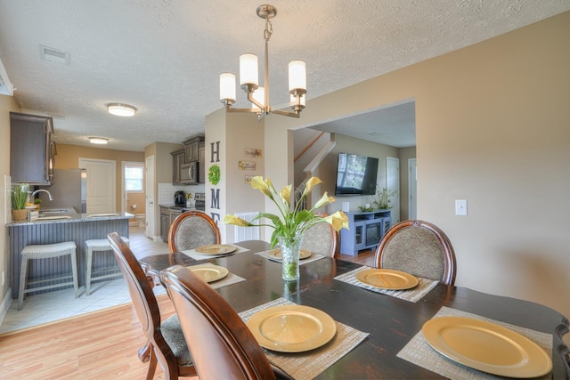 dining area with a textured ceiling, light wood-type flooring, sink, and a chandelier