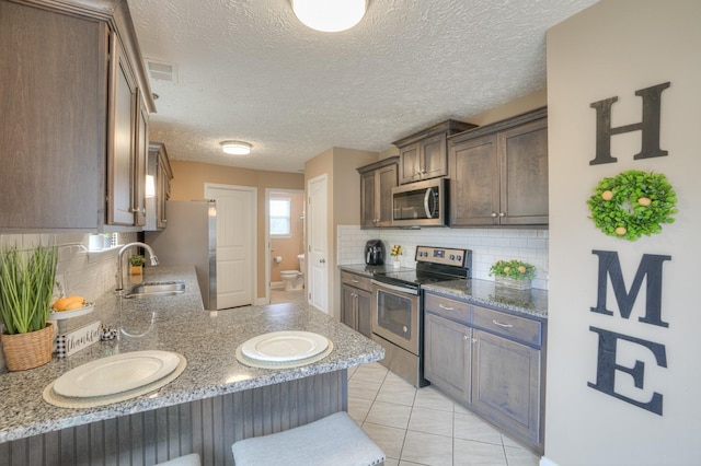 kitchen with appliances with stainless steel finishes, a textured ceiling, tasteful backsplash, and light tile patterned floors