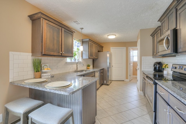 kitchen featuring sink, stainless steel appliances, light stone counters, pendant lighting, and a breakfast bar