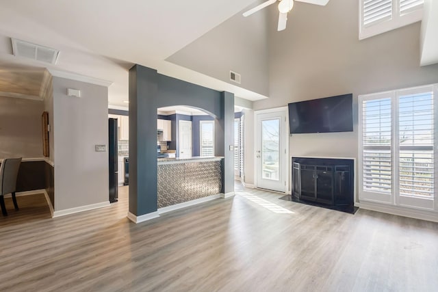 unfurnished living room featuring a towering ceiling, light hardwood / wood-style floors, and ceiling fan