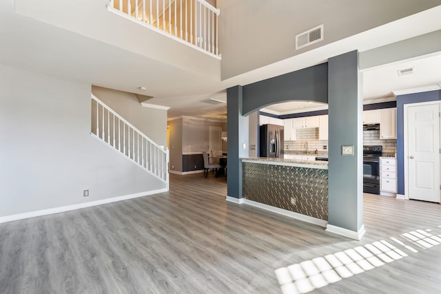 unfurnished living room with ornamental molding, sink, light hardwood / wood-style flooring, and a high ceiling