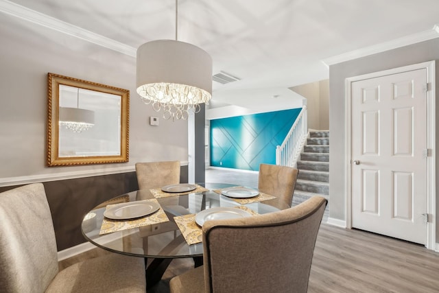 dining space with crown molding, an inviting chandelier, and light hardwood / wood-style flooring