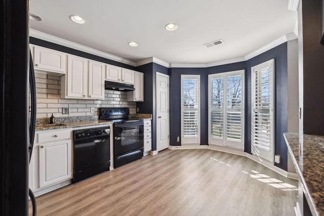 kitchen featuring white cabinetry, light hardwood / wood-style flooring, ornamental molding, dark stone counters, and black appliances