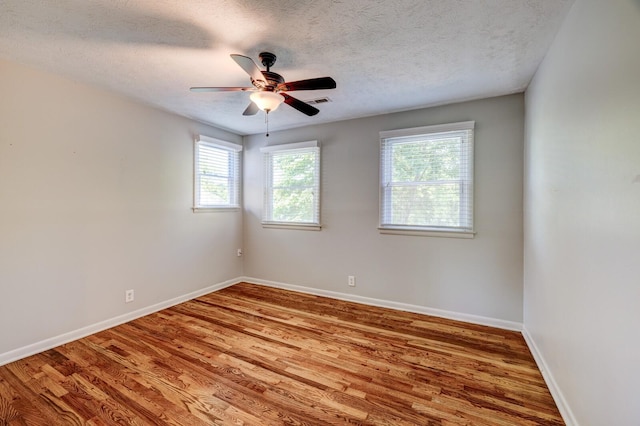 empty room with ceiling fan, a healthy amount of sunlight, a textured ceiling, and wood-type flooring