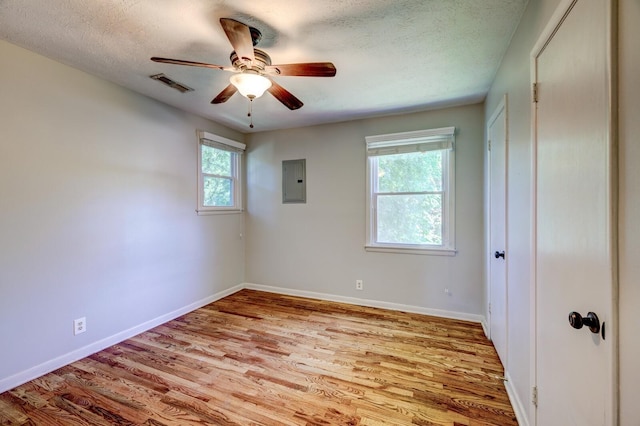 unfurnished room with electric panel, a wealth of natural light, light hardwood / wood-style flooring, and a textured ceiling