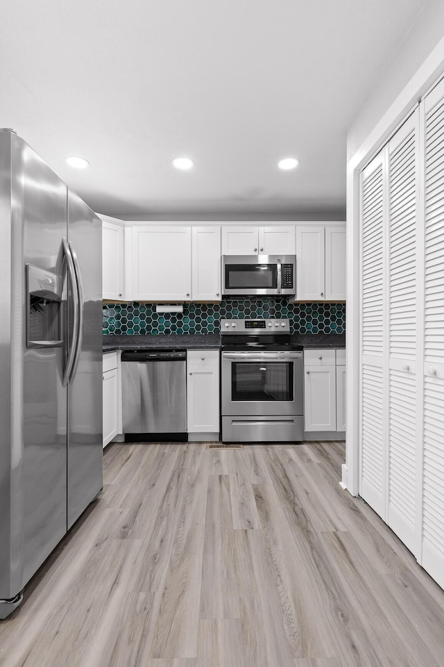 kitchen featuring white cabinets, decorative backsplash, stainless steel appliances, and light hardwood / wood-style flooring