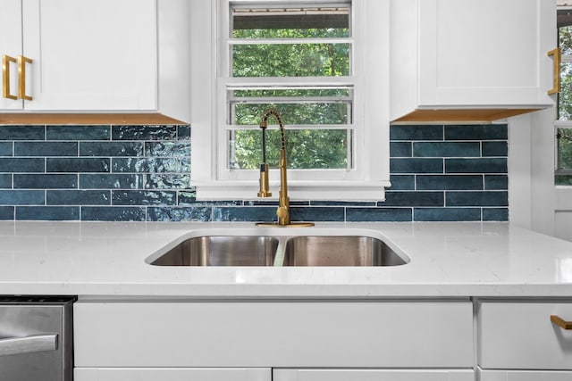 kitchen with light stone counters, white cabinetry, sink, and tasteful backsplash