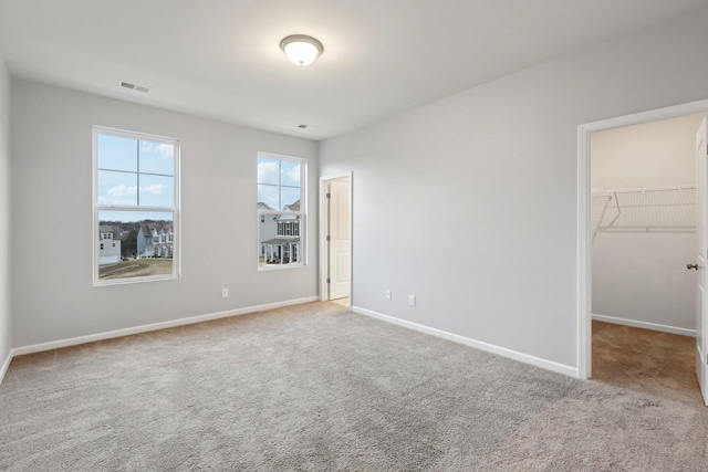 unfurnished bedroom with a spacious closet, a closet, and light colored carpet