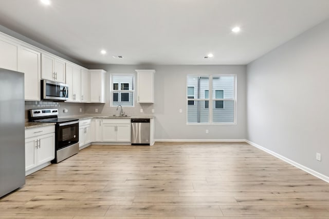 kitchen featuring appliances with stainless steel finishes, tasteful backsplash, sink, light hardwood / wood-style flooring, and white cabinets