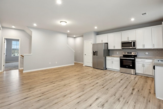 kitchen with white cabinets, light wood-type flooring, tasteful backsplash, light stone counters, and stainless steel appliances