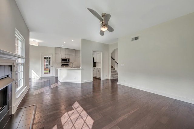 unfurnished living room with a fireplace, dark hardwood / wood-style flooring, ceiling fan, and a healthy amount of sunlight