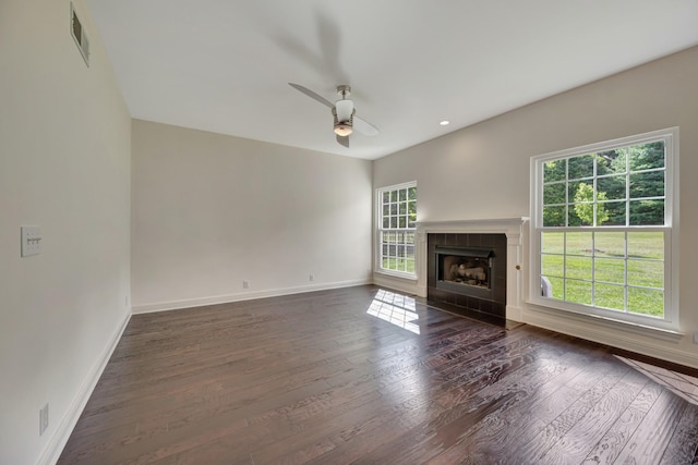 unfurnished living room featuring a healthy amount of sunlight, dark wood-type flooring, and a tiled fireplace