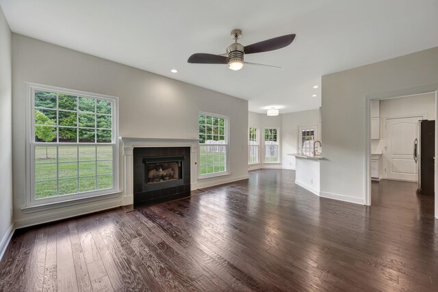 unfurnished living room with a tiled fireplace, ceiling fan, and dark hardwood / wood-style floors