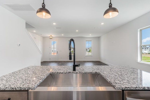 kitchen with light stone countertops, hardwood / wood-style floors, hanging light fixtures, and sink