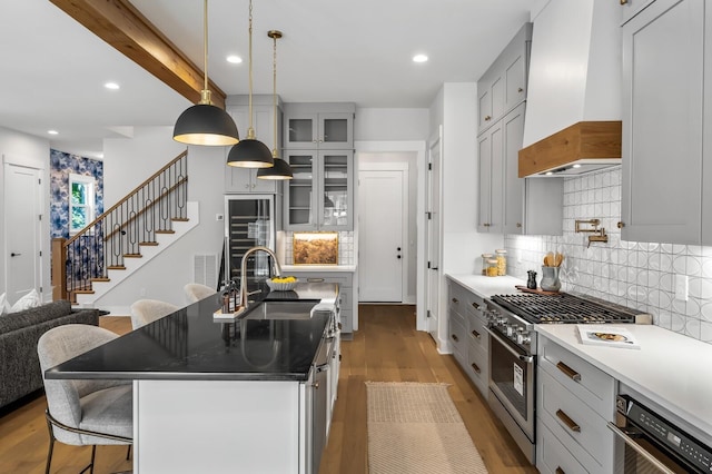 kitchen with stainless steel range, sink, premium range hood, a breakfast bar area, and a center island with sink