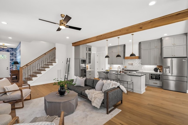 living room with ceiling fan, beam ceiling, light hardwood / wood-style floors, and sink