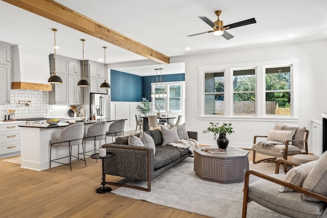 living room with beam ceiling, ceiling fan, sink, and light wood-type flooring