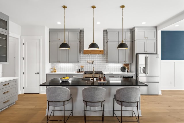 kitchen featuring sink, light hardwood / wood-style floors, stainless steel refrigerator with ice dispenser, and a center island with sink