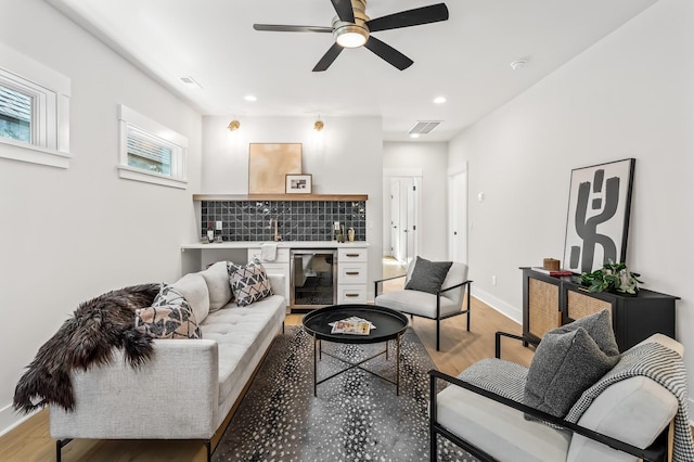 living room with wine cooler, ceiling fan, and light hardwood / wood-style flooring