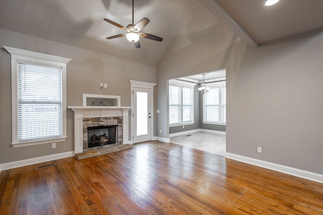 unfurnished living room featuring wood-type flooring, ceiling fan with notable chandelier, a stone fireplace, and lofted ceiling