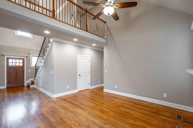 unfurnished living room with ceiling fan, wood-type flooring, and a high ceiling