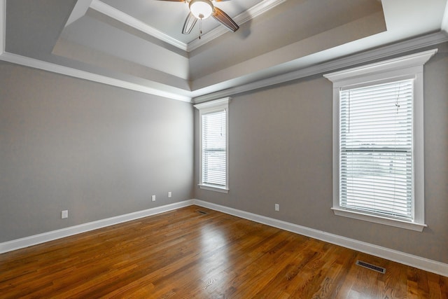 empty room with dark wood-type flooring, a raised ceiling, ceiling fan, and ornamental molding