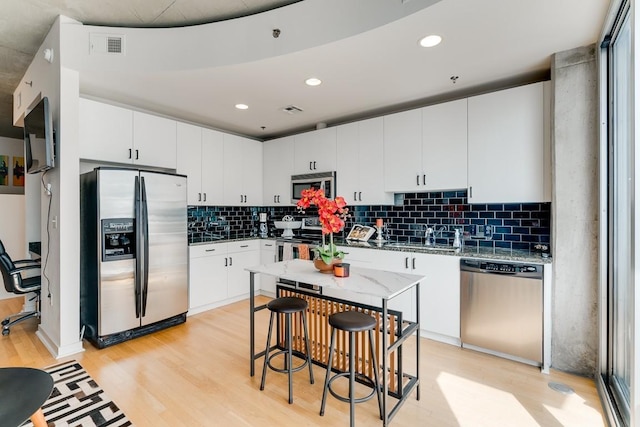 kitchen with appliances with stainless steel finishes, sink, white cabinets, light hardwood / wood-style floors, and a kitchen island