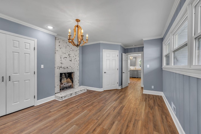 unfurnished living room featuring a stone fireplace, wood-type flooring, crown molding, and a chandelier