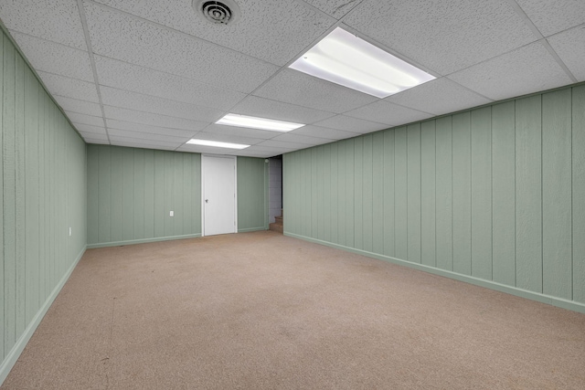 spare room featuring a drop ceiling, light carpet, and wooden walls