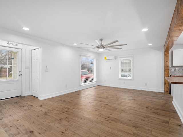 unfurnished living room with hardwood / wood-style flooring, an AC wall unit, and a healthy amount of sunlight