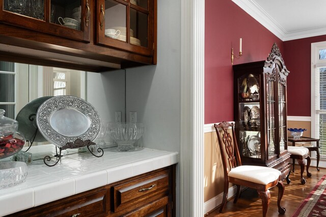 bar with dark wood-type flooring, tile countertops, and crown molding