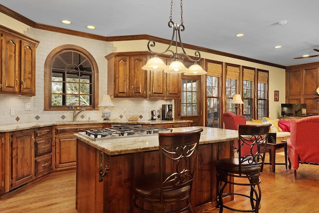 kitchen featuring stainless steel gas cooktop, sink, pendant lighting, light hardwood / wood-style floors, and a kitchen island