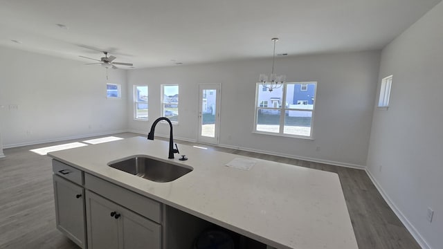 kitchen with a center island with sink, decorative light fixtures, light stone countertops, and sink