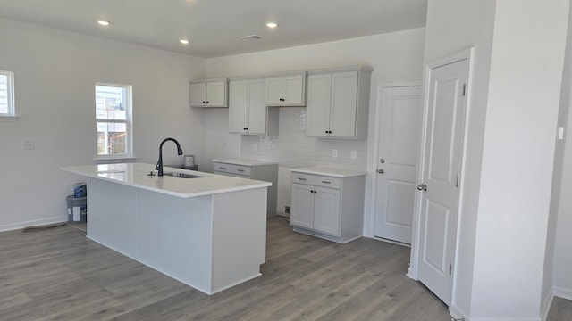 kitchen featuring light wood-type flooring, sink, tasteful backsplash, and an island with sink