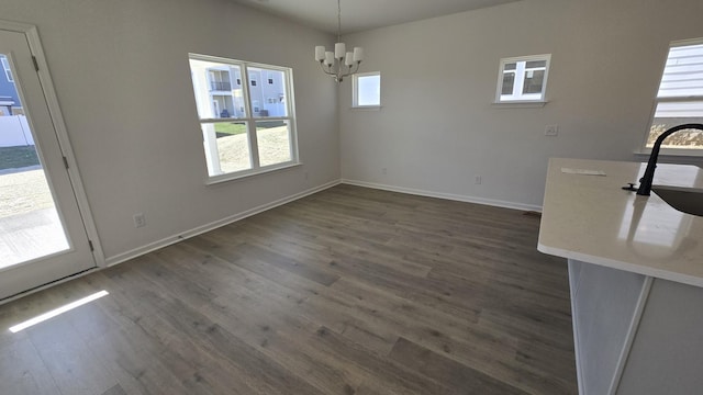 unfurnished dining area with dark hardwood / wood-style floors, sink, a wealth of natural light, and an inviting chandelier