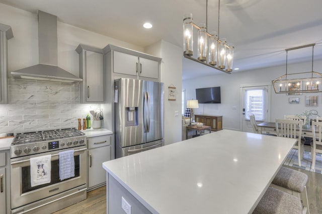 kitchen featuring wall chimney range hood, decorative backsplash, gray cabinets, appliances with stainless steel finishes, and decorative light fixtures